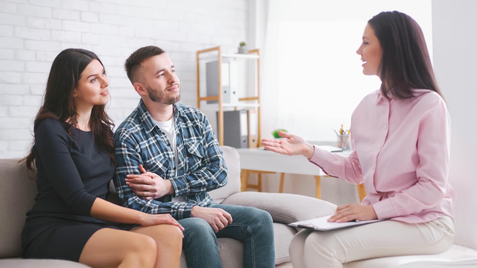 A marriage and family therapist gesturing as she speaks to a couple seated together on a sofa in her office
