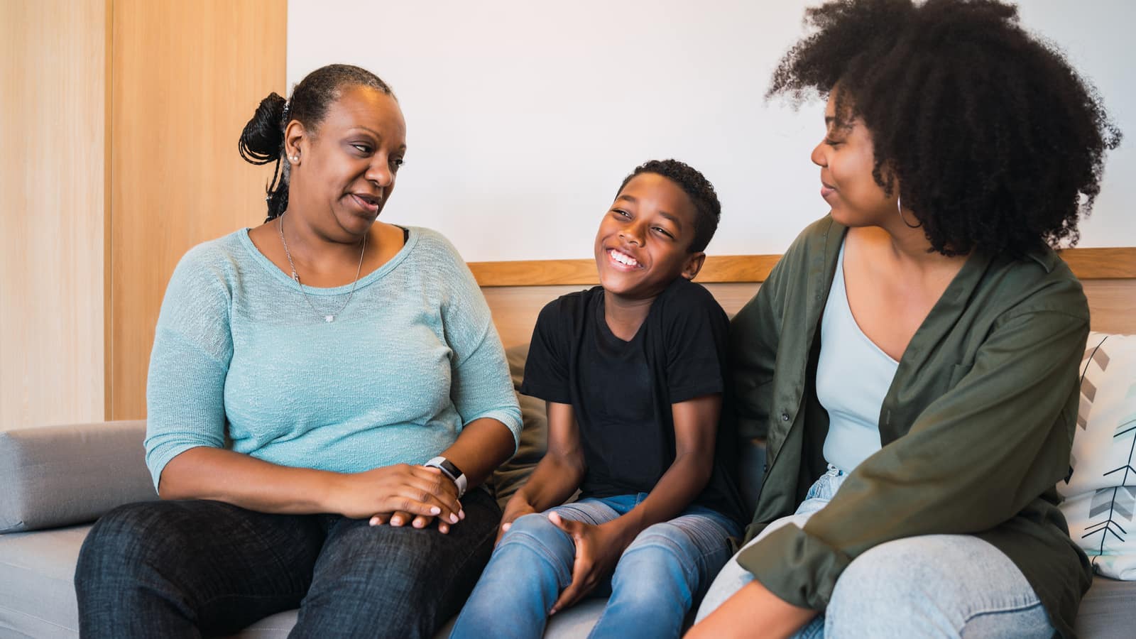 A grandmother, mother and young son sitting together at home, talking and laughing