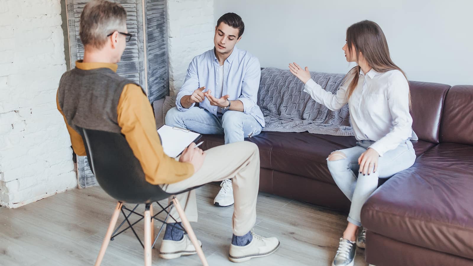 A couple seated apart on facing sofas while an experienced therapist takes notes from a chair between them